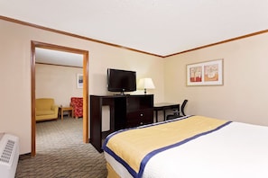 A hotel room with a bed, a desk with a computer, a television, a chair, and a lamp.