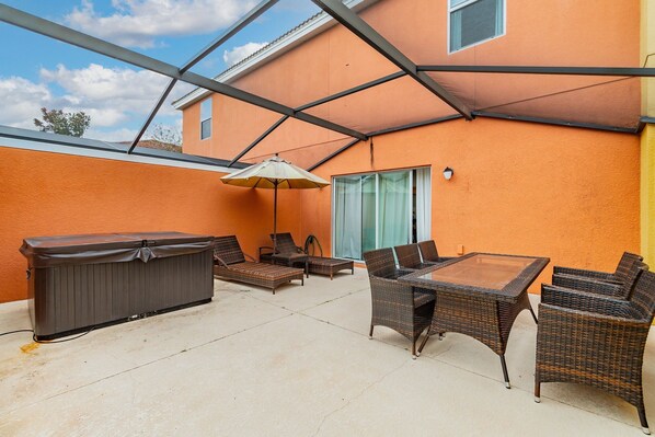 An outdoor patio with a hot tub, wicker furniture, and a glass door leading to a covered area. - Cozy Villa 3bd/3ba - King Bed - Private Jacuzzi (Kissimmee)