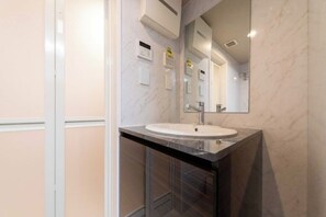 A bathroom with a white sink, a mirror, and a marble wall. - LaVie Hatsudai (Tokyo)