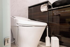 A modern bathroom with a white toilet, a dark wood vanity, and a glass shower enclosure. - LaVie Hatsudai (Tokyo)