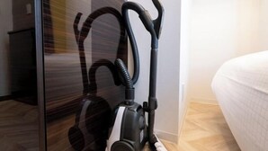 A vacuum cleaner near a glass door and a bed with a white cover. - LaVie Hatsudai (Tokyo)