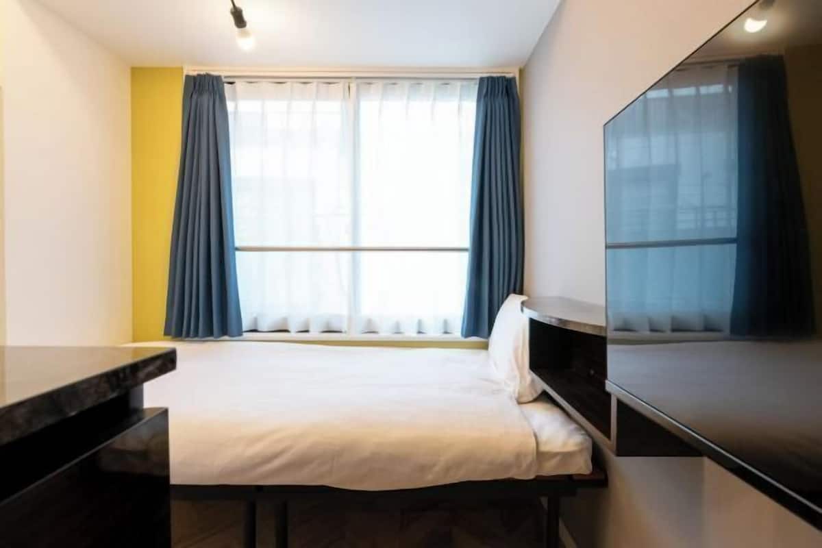 A hotel room with a bed, a desk, a TV, and a window with curtains.