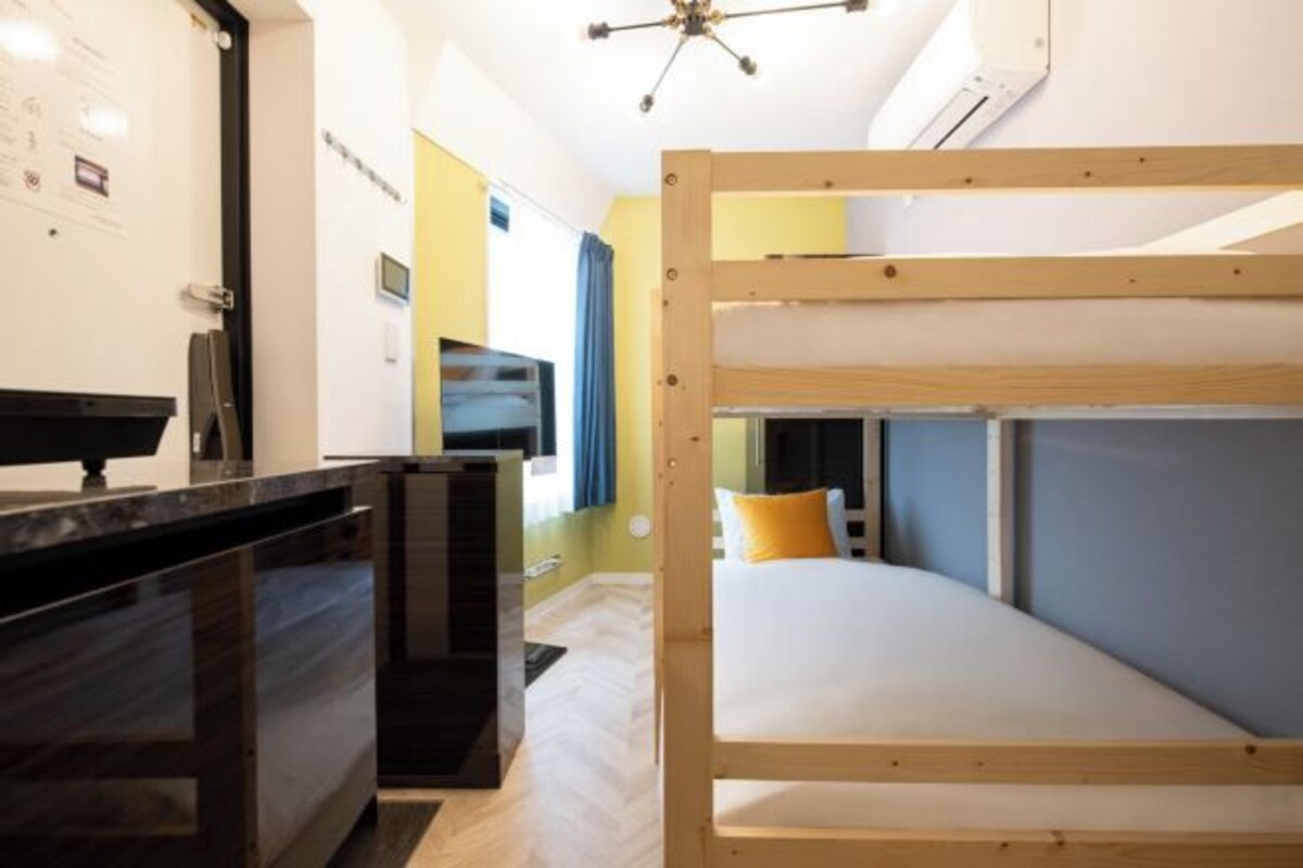 A bunk bed room with a desk, a flat-screen TV, and a ceiling fan.