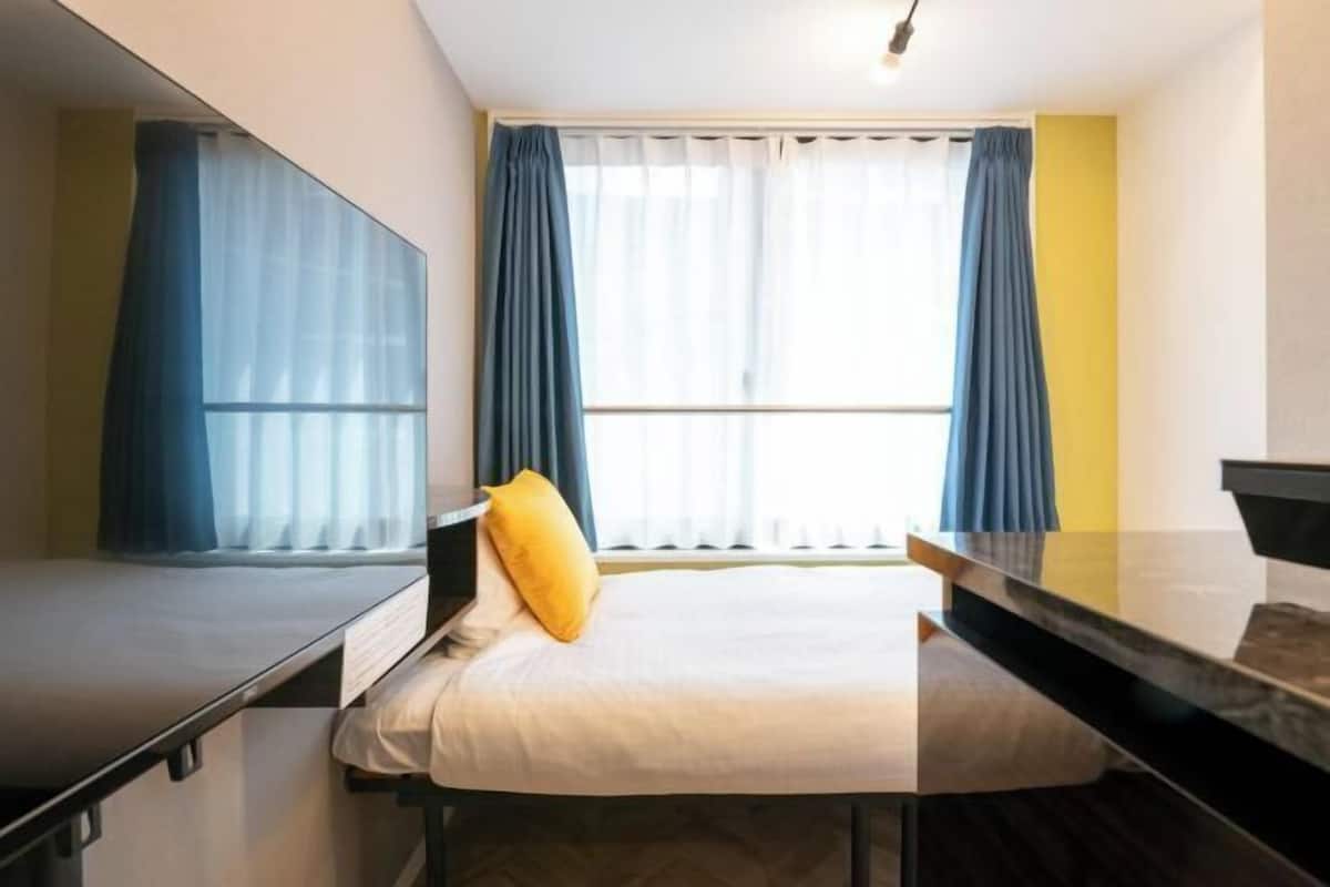 A hotel room with a bed, a desk, and a window with curtains.