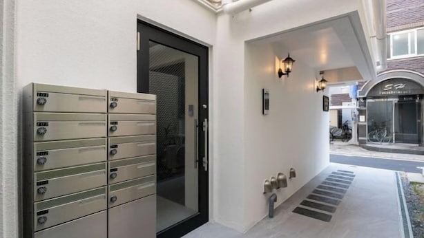 A building entrance with a door, mailboxes, and a pathway leading to a bike shop. - LaVie Hatsudai (Tokyo)