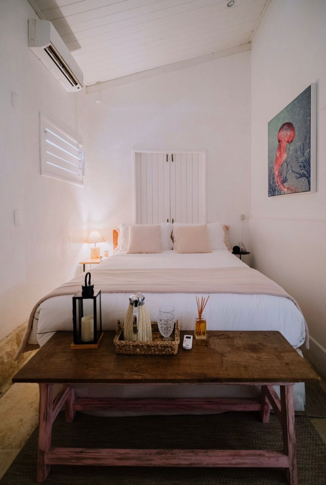 Quarto com cama, mesa de cabeceira, abajur e um quadro na parede.