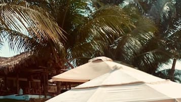 Um espaço de descanso à beira-mar com guarda-sóis de palha, cadeiras de lounge e um buffet com petiscos e bebidas.