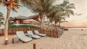 A beachside lounge area with lounge chairs, a thatched-roof structure, and palm trees.