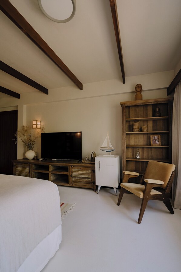 Un dormitorio con una cama, un televisor, una mesita de noche blanca, una estantería y una silla.