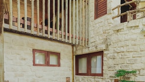 A stone-walled room with a wooden balcony, a bathtub, and a small window.