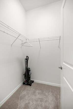 Une petite pièce recouverte de moquette, avec un aspirateur, une porte et un étendoir à linge.