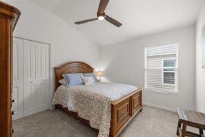 Une chambre avec un lit en bois, un ventilateur de plafond, une fenêtre avec des stores et une porte.