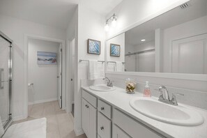 Une salle de bain moderne avec deux lavabos, un grand miroir et une douche à l’italienne.