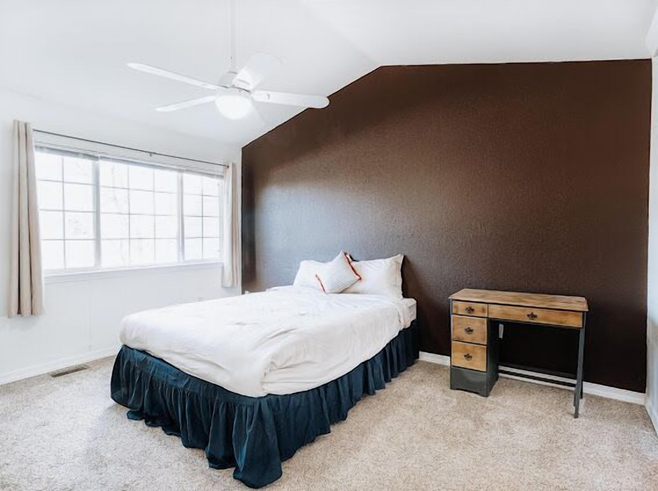 Une chambre à coucher avec un lit, un bureau, un ventilateur de plafond et une fenêtre.