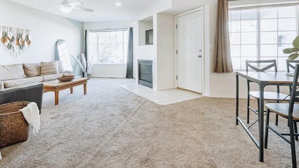 A spacious living room with a sofa, coffee table, and dining table. There is a fireplace and a large window with curtains.