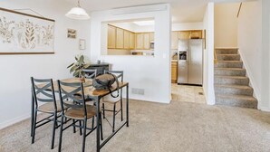A dining area with a table and chairs, a hanging light fixture, and a kitchen in the background.