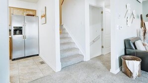 A modern kitchen with a stainless steel refrigerator, a wooden cabinet, and a staircase leading to another level.