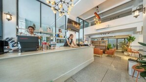 A modern reception area with a counter, two staff members, and a seating area with chairs and plants. - SHIN Hotel Victory Monument (Bangkok)