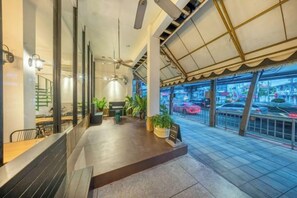 A spacious indoor area with a ceiling fan, a seating area with tables, and a view of the street through large windows. - SHIN Hotel Victory Monument (Bangkok)