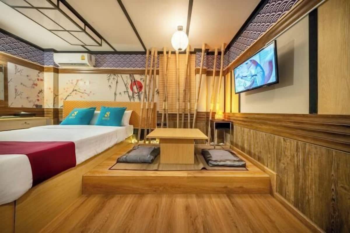 A modern hotel room with a wooden bed, a small table, and a TV mounted on the wall.