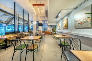 A restaurant interior with tables and chairs, a counter, and a view through large windows. - SHIN Hotel Victory Monument (Bangkok)