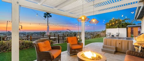 An outdoor patio with wicker chairs, a fire pit, and a view of the sunset.