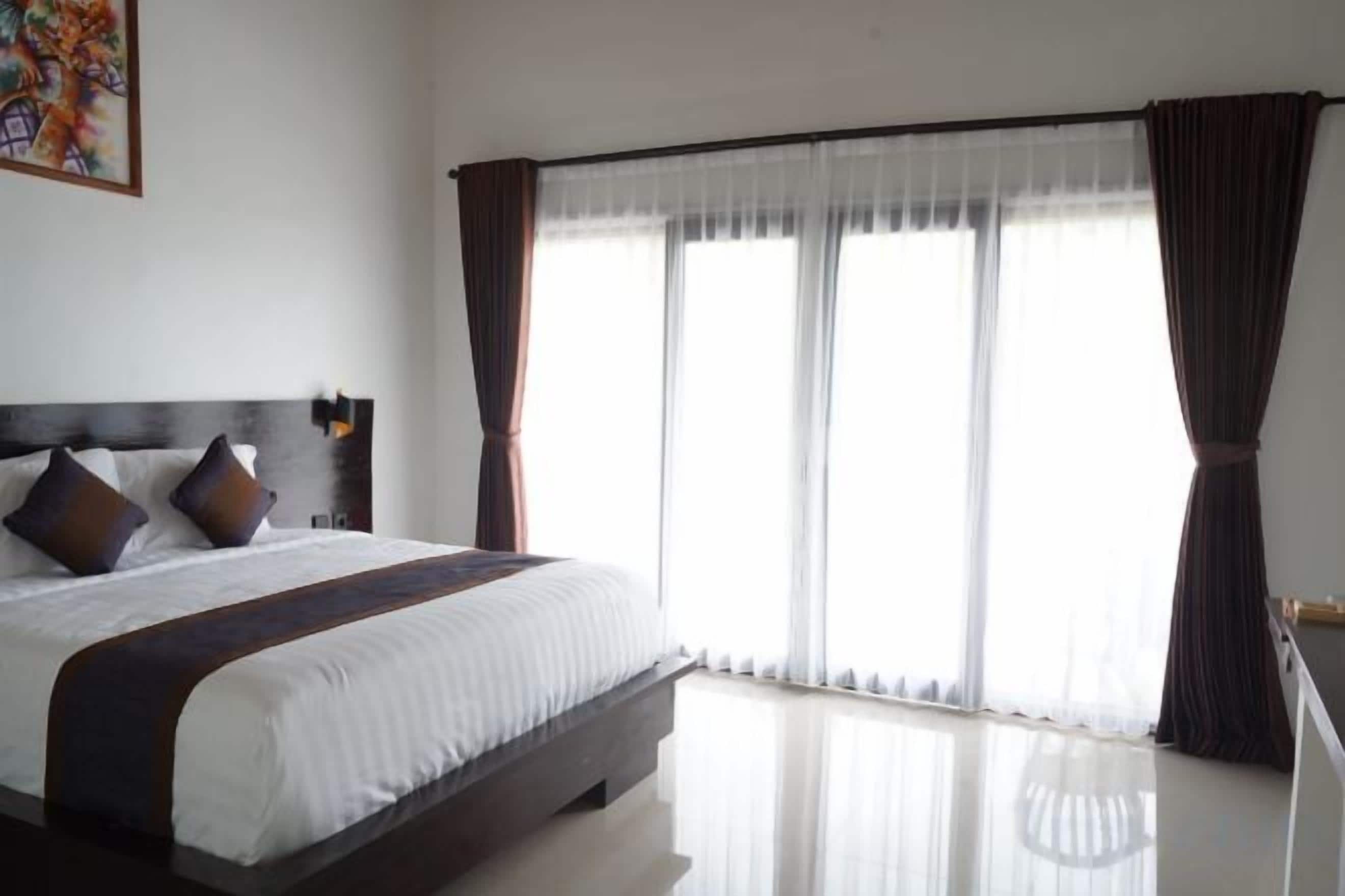 A hotel room with a large bed, a window with curtains, and a wall-mounted light fixture.