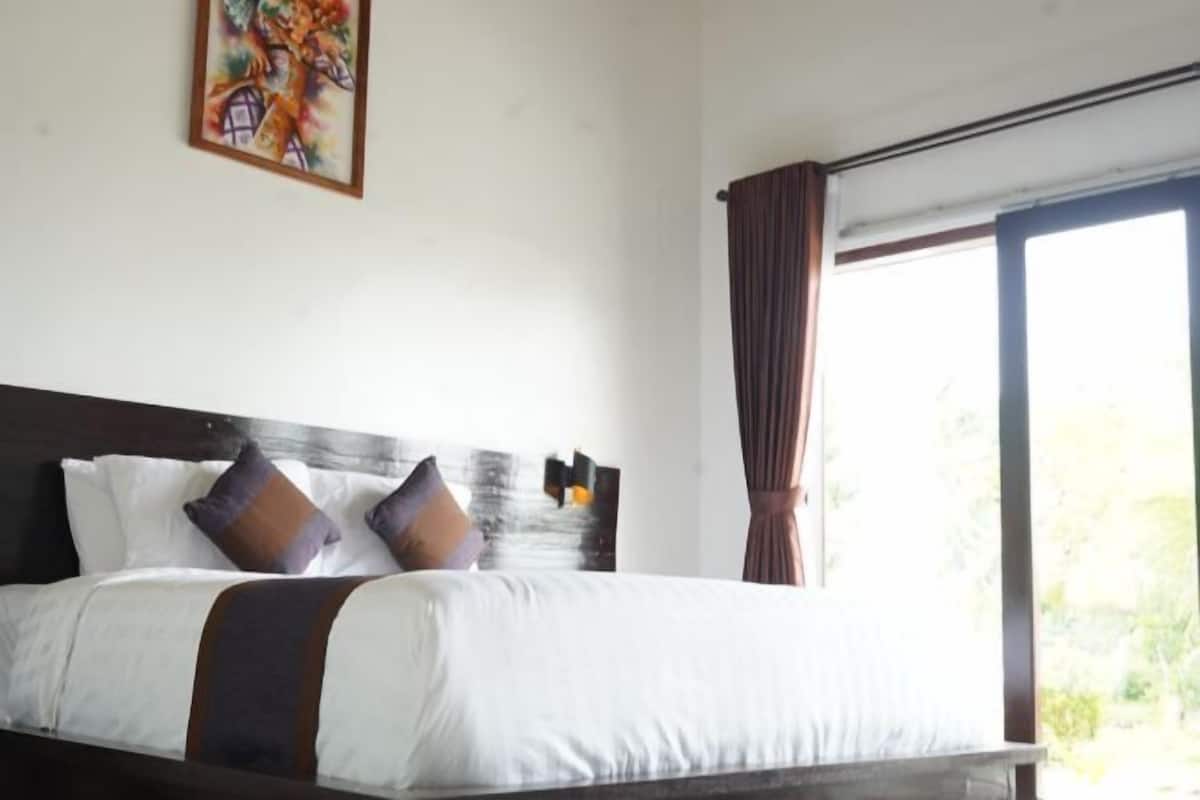 A neatly made bed with white and brown bedding, a dark headboard, and a painting on the wall.