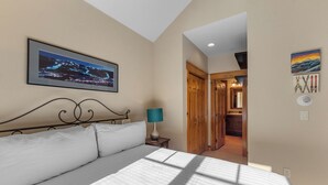 A bedroom with a large bed, a nightstand with a lamp, a framed picture on the wall, and a hallway leading to a wooden door. - Settlers Creek #6559 (Keystone)