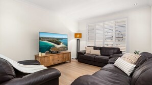 Un salon doté d’un grand téléviseur à écran plat, d’un meuble TV en bois, d’un canapé en cuir foncé et d’un lampadaire.