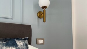A bedroom with a bed, a bedside table, a wall-mounted light fixture, and a power outlet. - Comfortable and stylish room near central station and airport (Napoli)