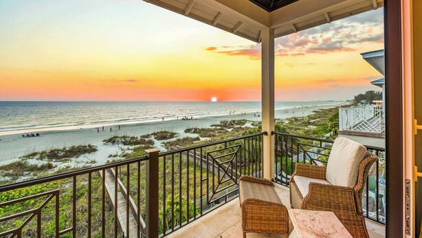 Ein Balkon mit Korbmöbeln mit Blick auf einen Strand bei Sonnenuntergang.