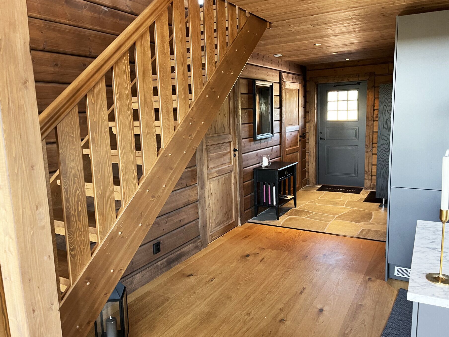 A wooden staircase leading to a room with a stone floor, a small table, and a door.