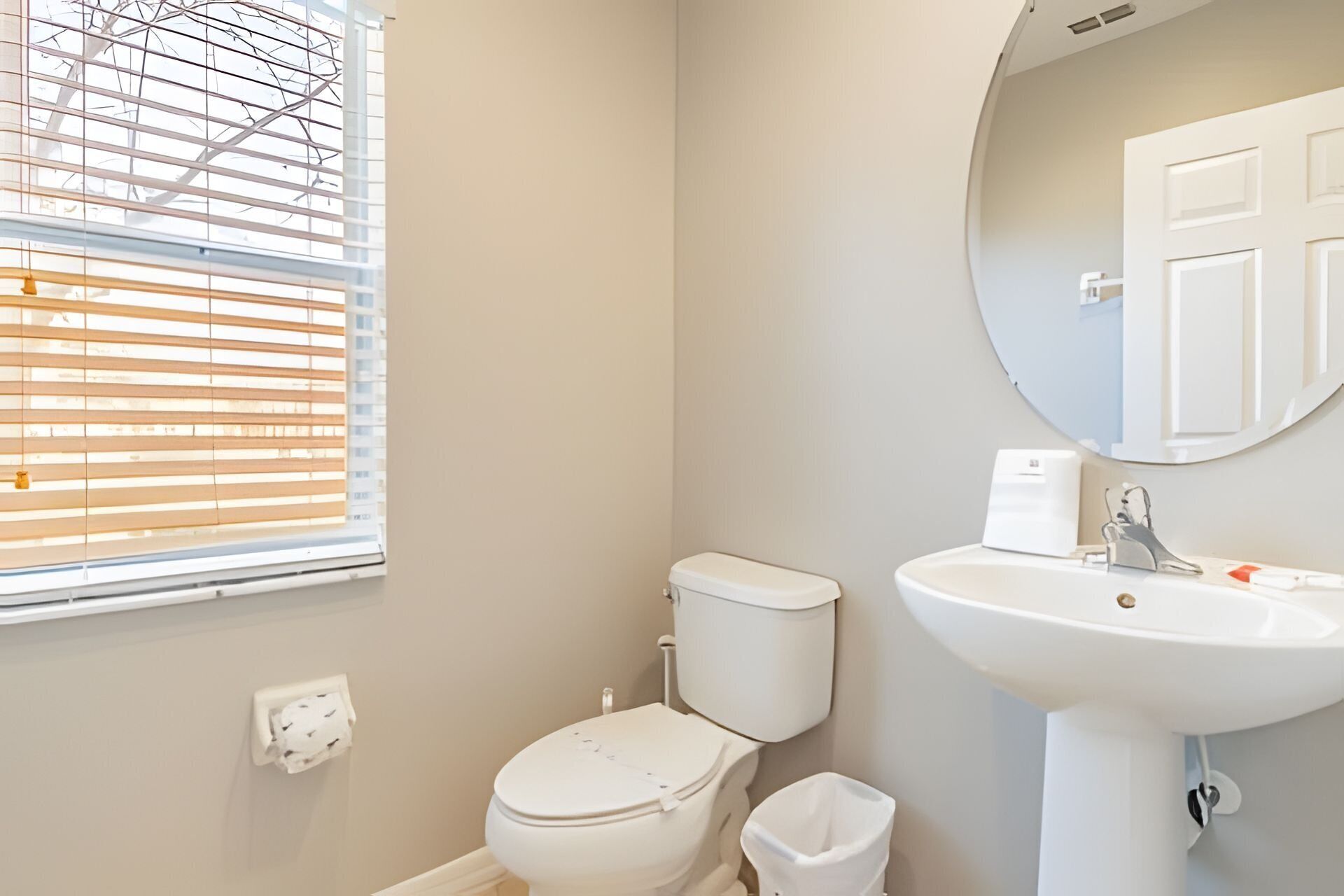 Une salle de bain avec des toilettes, un lavabo et une fenêtre équipée de stores.