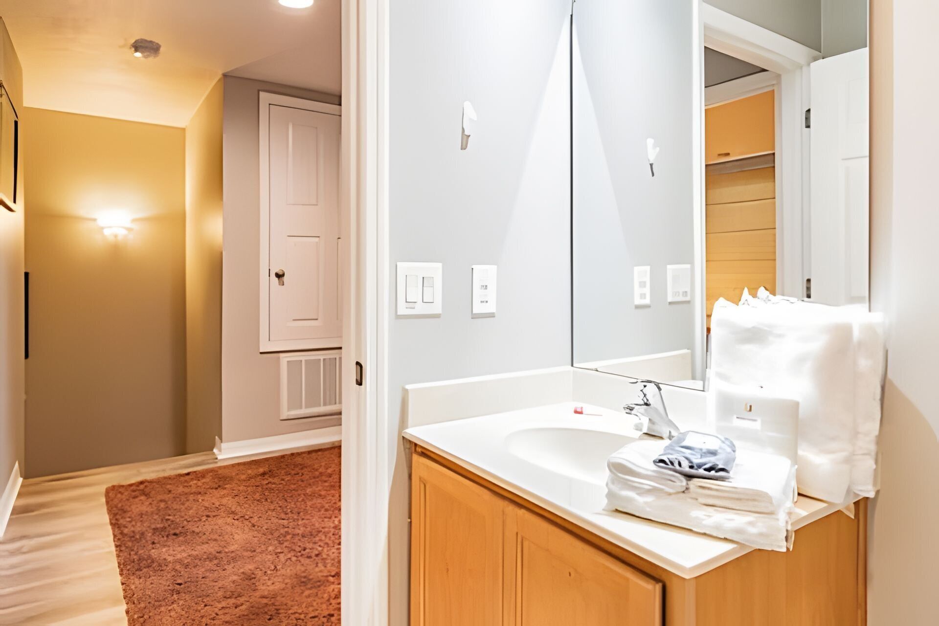 A modern bathroom with a large mirror, white sink, and wooden cabinets.