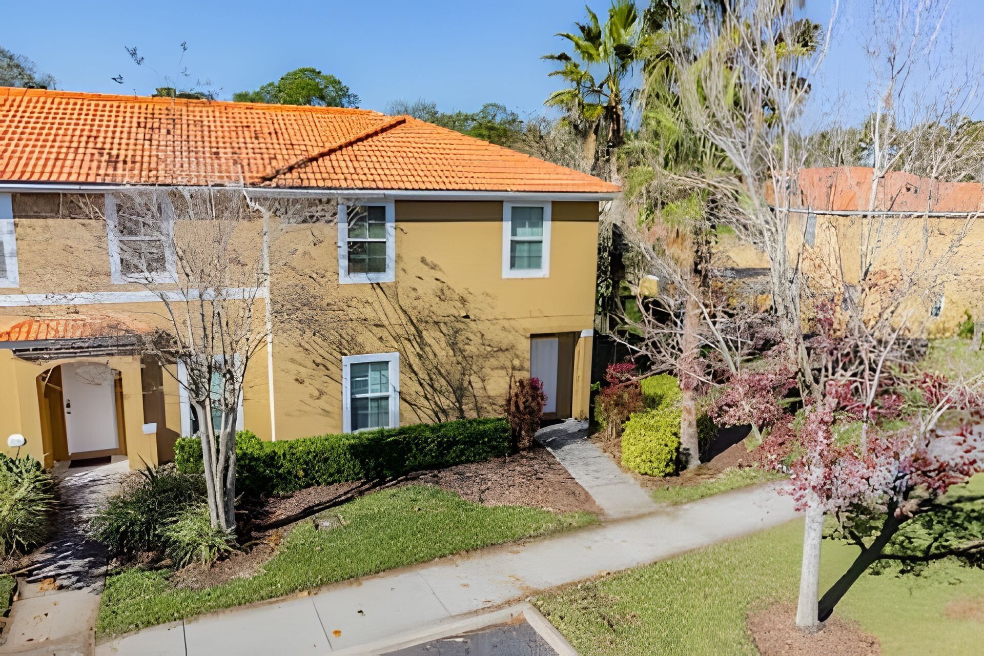 A two-story building with a yellow facade and orange-tiled roof. There is a small front yard with a pathway leading to the entrance.