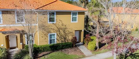 A two-story building with a yellow facade and orange-tiled roof. There is a small front yard with a pathway leading to the entrance.