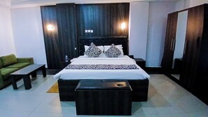 A hotel room with a bed, a green sofa, a small table, and a wardrobe. - AAHotel Abuja (Abuja)