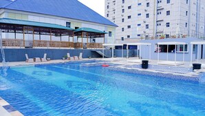 A swimming pool with a tiled deck, lounge chairs, and a covered seating area. - AAHotel Abuja (Abuja)