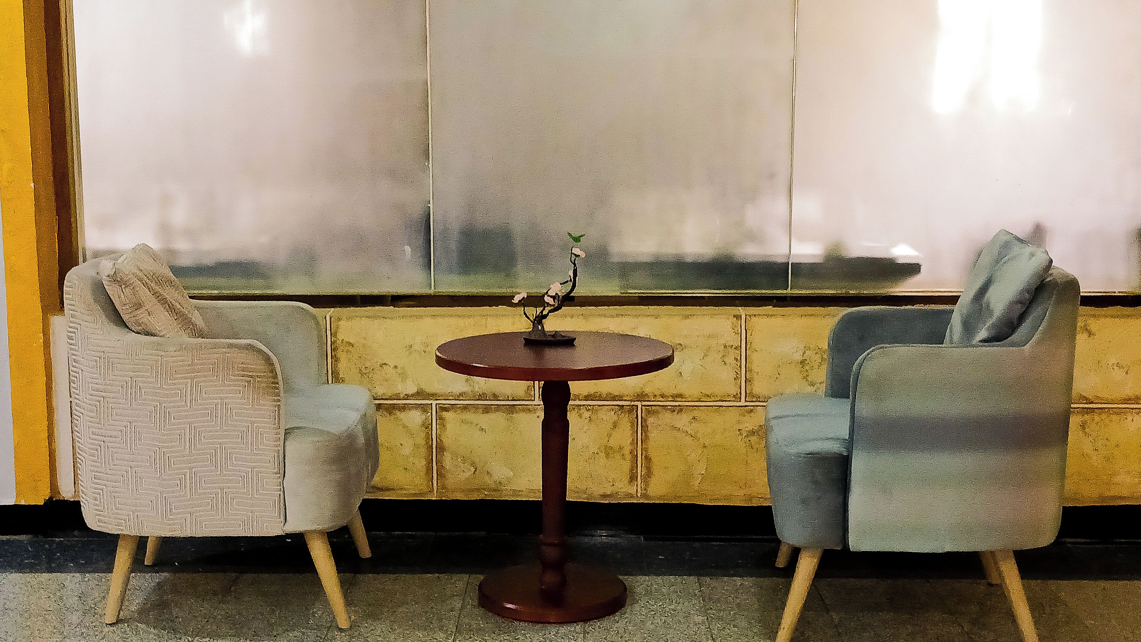 Dos sillones y una pequeña mesa redonda con un objeto decorativo en una habitación con un ventanal grande.