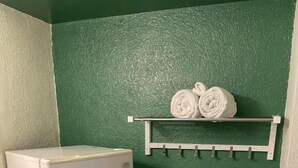 Une pièce d’angle avec un réfrigérateur blanc, un mur vert et un porte-serviettes sur lequel sont posés deux serviettes enroulées.