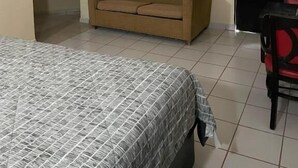 Une pièce comprenant un lit, un canapé, un téléviseur fixé au mur, un ventilateur de plafond et une porte.