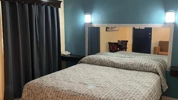 Une chambre d’hôtel avec un lit, un ventilateur de plafond, une table de chevet, un miroir et une fenêtre avec des rideaux.