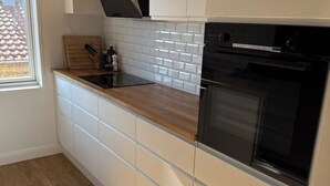 Et moderne køkken med hvide skabe, en træbordplade, en sort ovn og et vindue der giver naturligt lys.