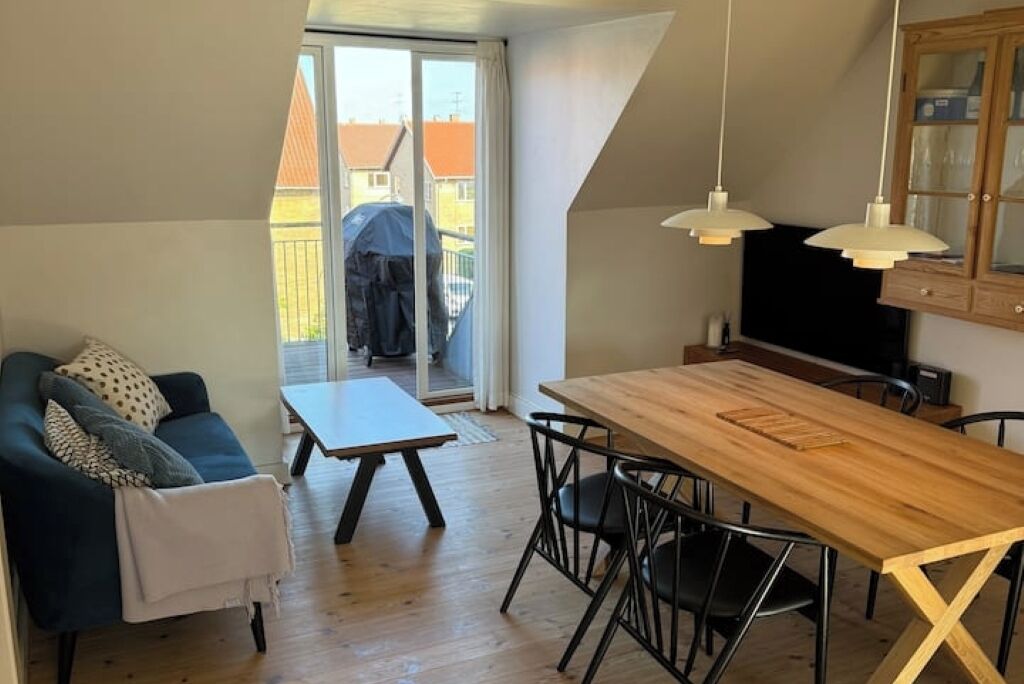 Un espace de vie compact comprenant un canapé, une table à manger avec des chaises, un meuble en bois et une porte-fenêtre coulissante donnant sur un espace extérieur.