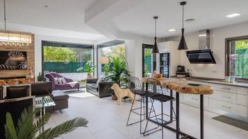 A modern kitchen with a bar area, large windows, and a dog in the living area.