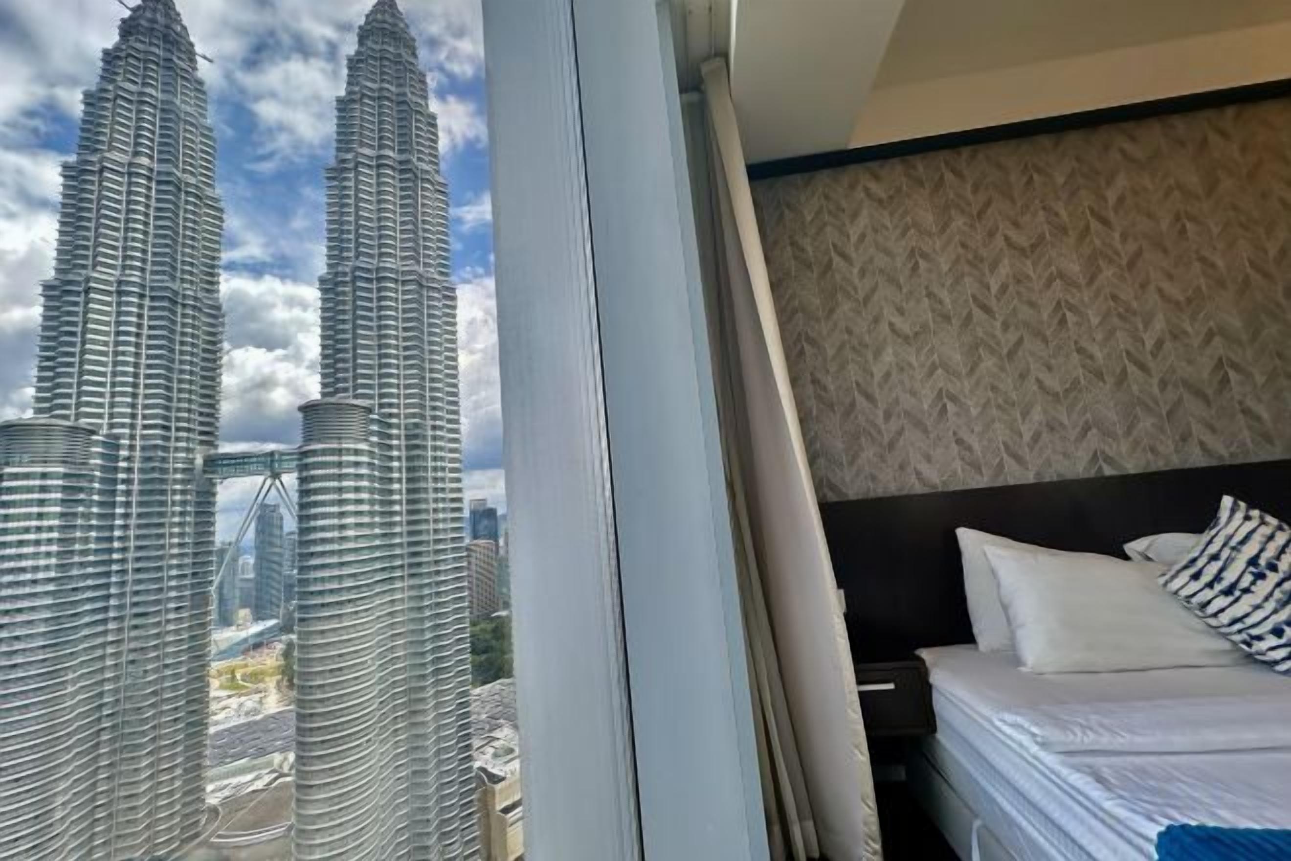 A hotel room with a bed, a window, and a view of the Petronas Twin Towers.