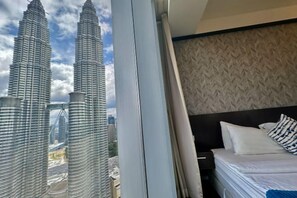 A hotel room with a bed, a window, and a view of the Petronas Twin Towers. - Queen Suites Tropicana The Residence by KLCC (Kuala Lumpur)