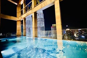 A rooftop pool with a view of illuminated skyscrapers at night. - Queen Suites Tropicana The Residence by KLCC (Kuala Lumpur)
