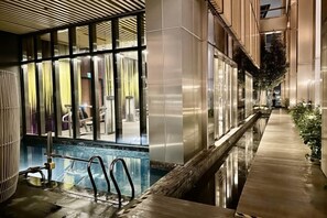 Ein moderner Hotelkorridor mit Poolbereich, Glasüren und einer Holzterrasse.